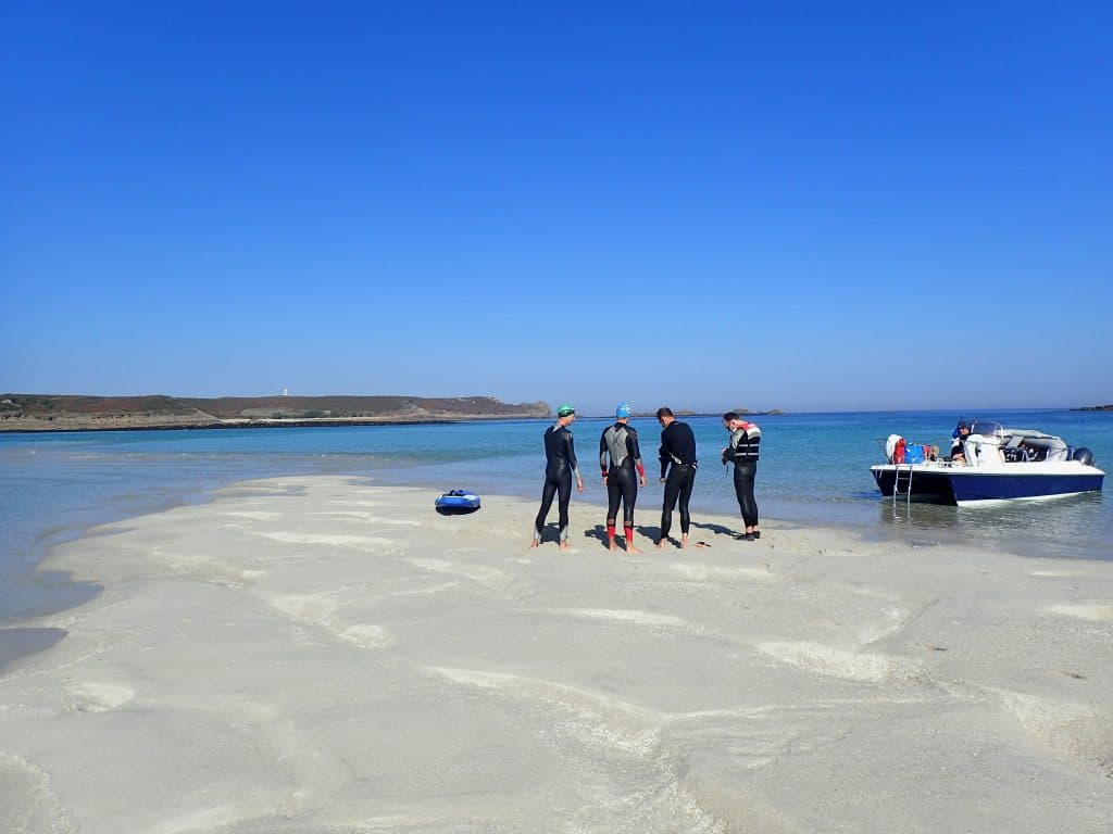 Swimmers in wetsuits on a sandbar in the Scilly Isles