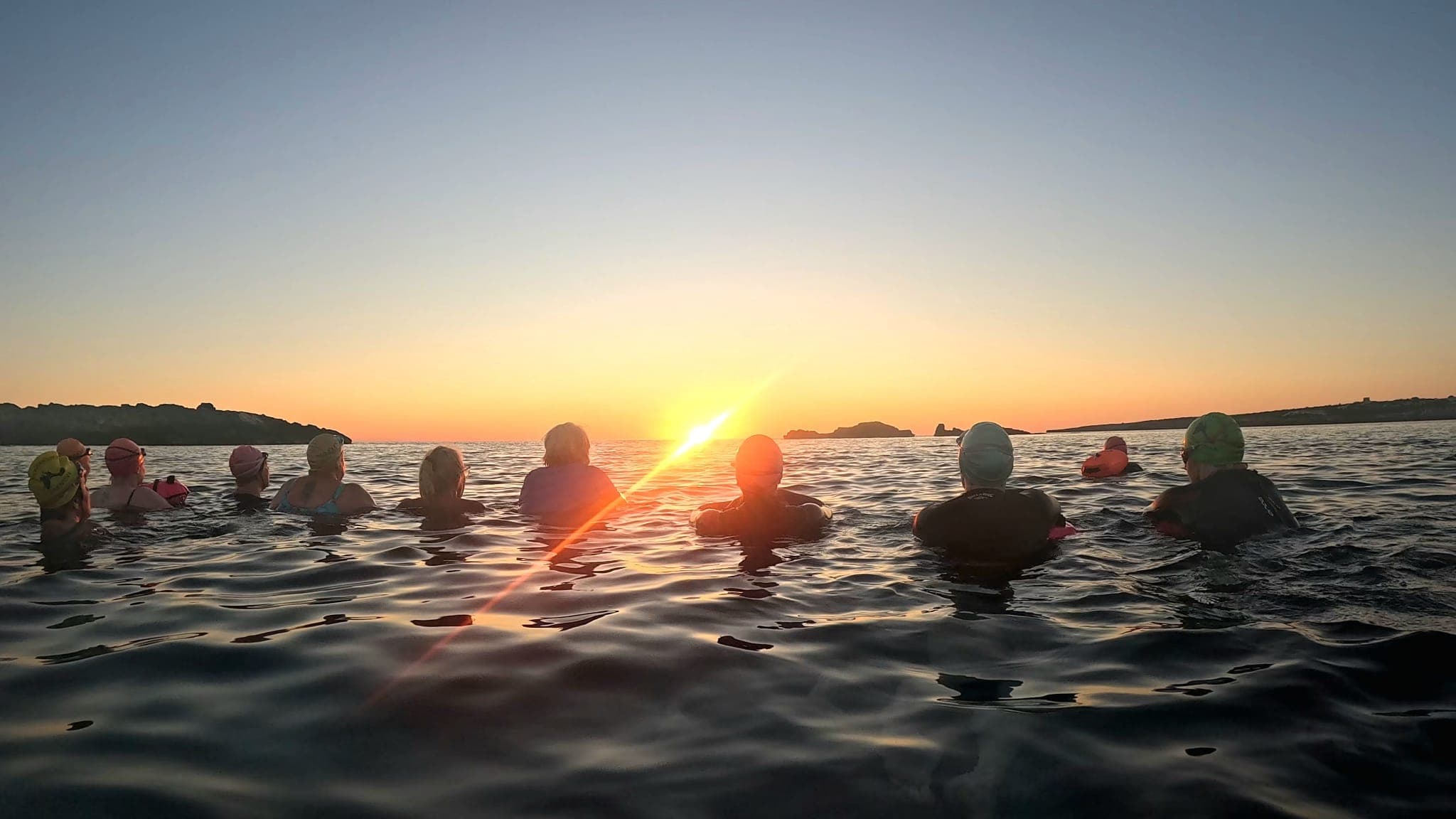 Swimmers hold hands and watch sunrise
