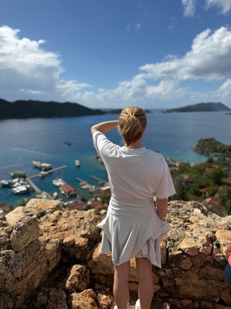 A woman dressed in white sweatshirt and shorts looking out over the sea from clifftop in Turkey