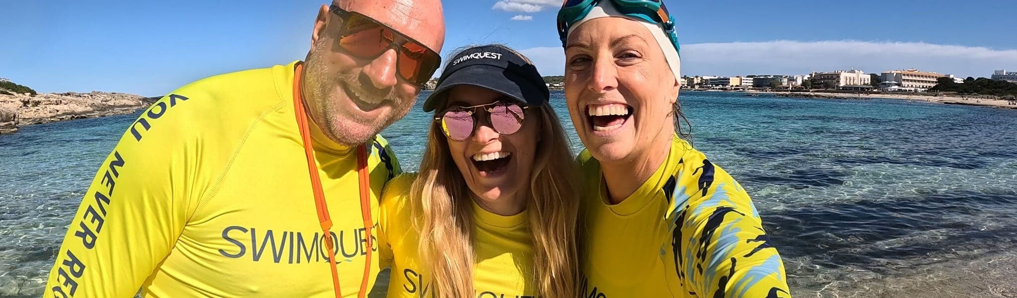 Three swimmers wearing rash vests on a beach