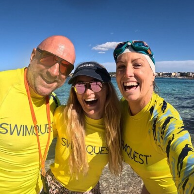 Three swimmers wearing rash vests on a beach