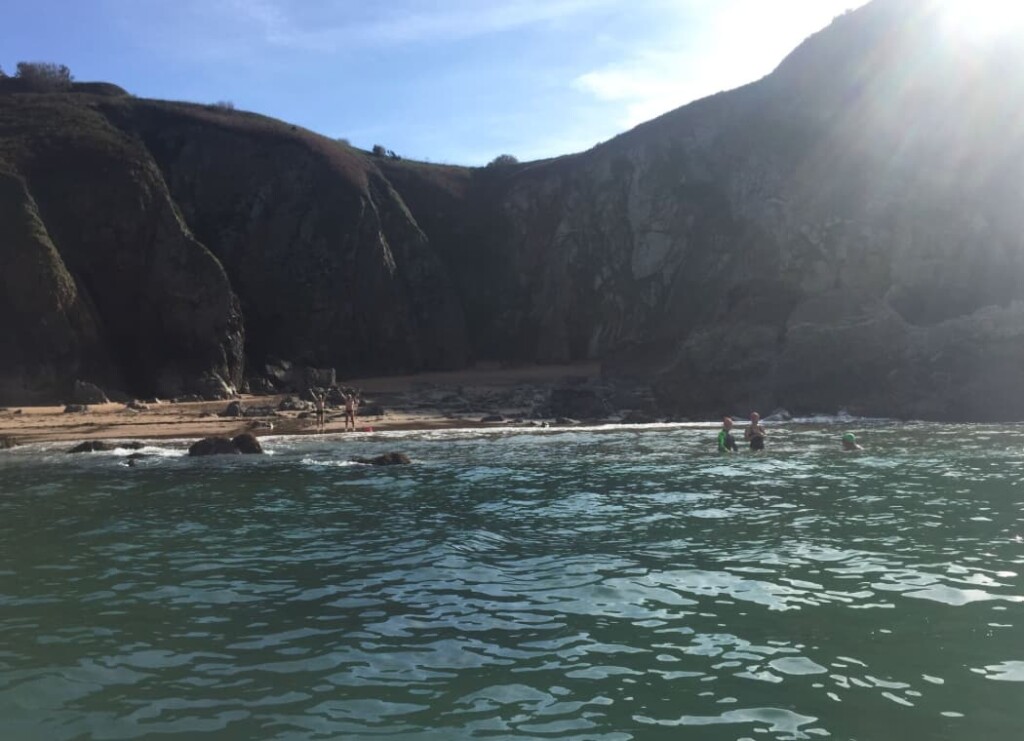 Sea and cliffs in Jersey with swimmers in foreground